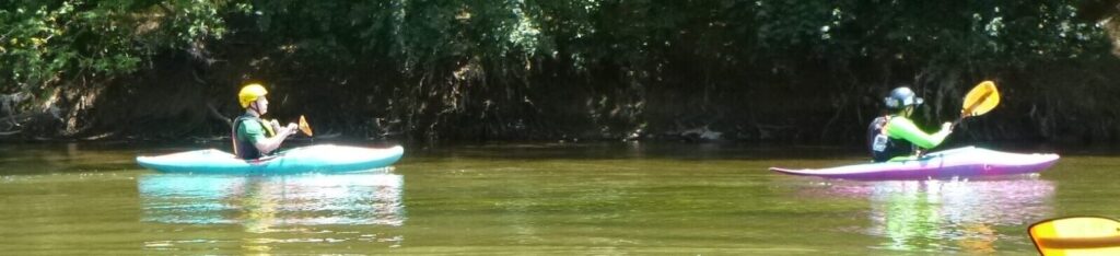 Side view image: Two kayakers on a creek. Rear kayaker is following guide kayaker.