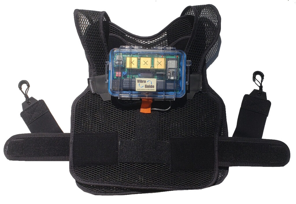 Image showing front view of a VibroGuide vest made out of a light mesh material. A VibroGuide electronics box is mounted on the upper chest and is made of clear plastic that exposes the electronics inside.  There are elastic straps sticking out from both left and right sides.